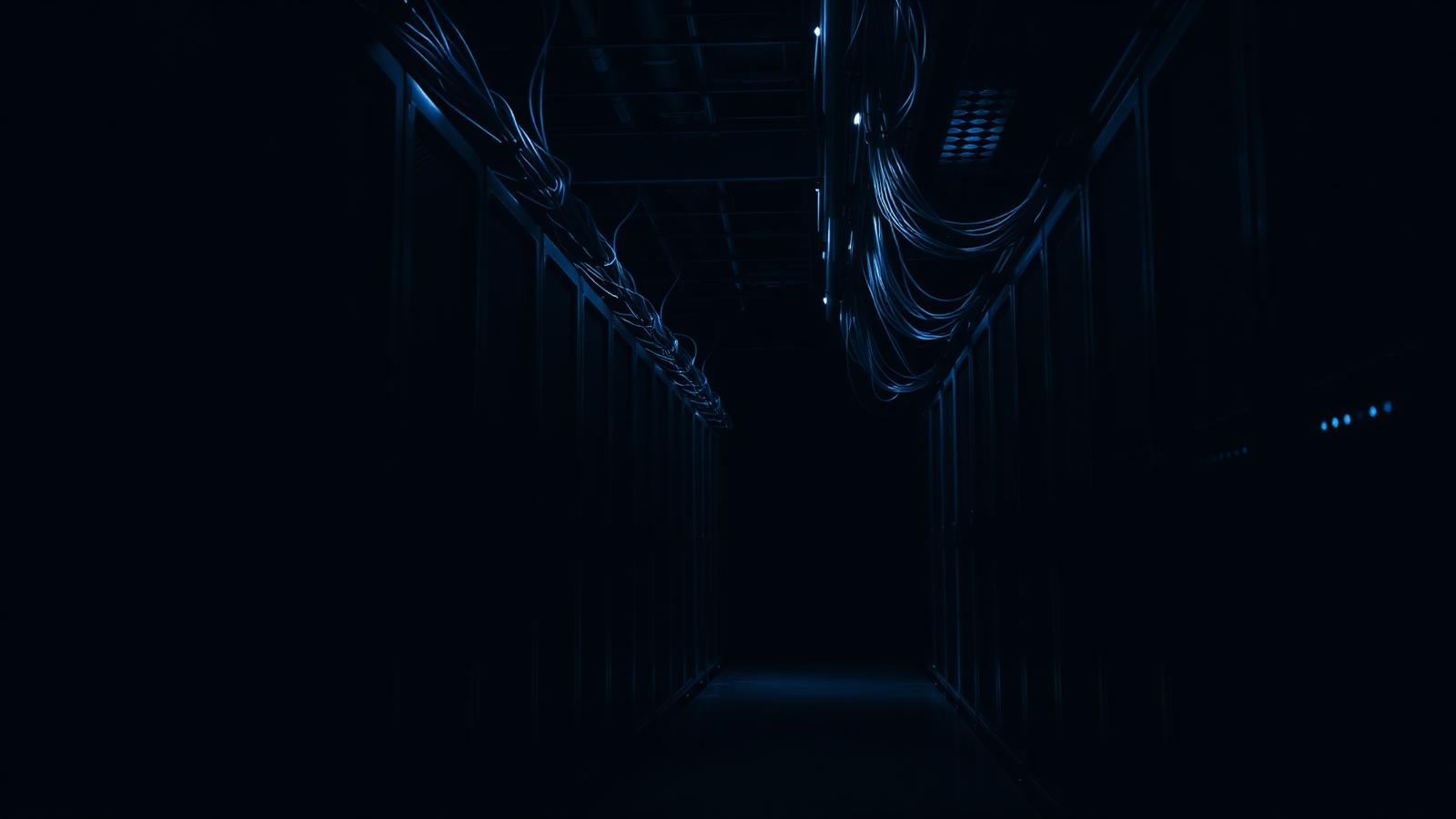 Corredor de racks de rede com cabeamento estruturado em ambiente escuro